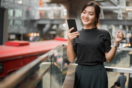 Happy asian woman looking at her phone in the cityの写真素材