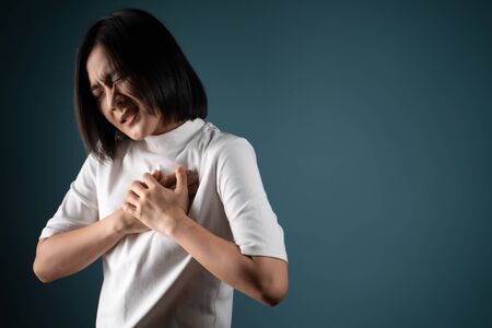 Asian woman was sick with chest pain and standing isolated over blue background. Health care concepts.の写真素材