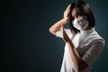 Don't touch me. Asian woman wearing hygiene mask panic and disguted showing hand stop sign and standing isolated over blue background. Health care concepts.の写真素材