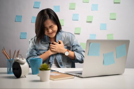 Asian woman working on a laptop was sick with chest pain sitting at home office. WFH. Work from home. Prevention Coronavirus COVID-19 concept.の写真素材