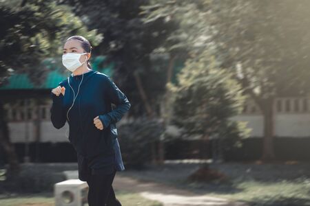 Portrait of Asian woman running at village park listening to music and wearing maskの写真素材