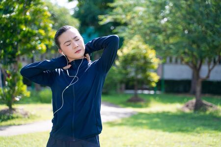 Portrait of Asian woman wearing earphones listening to music was sick with body pain at park. Woman exercise at park suffering from body pain.の写真素材