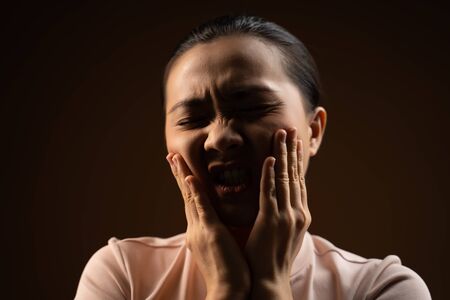 Asian woman was sick with toothache touching her cheek and standing isolated on beige background. Low key.の写真素材
