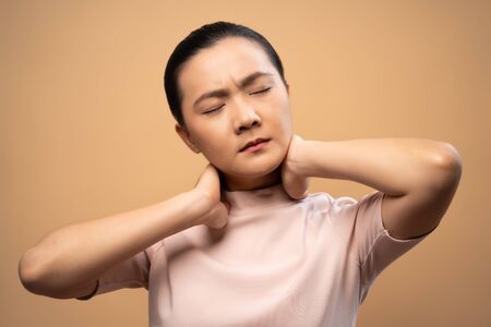 Asian woman was sick with body pain touching her body and standing isolated on beige background.の写真素材