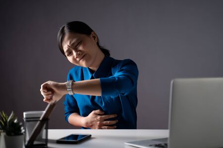Asian woman in blue shirt working on a laptop was sick with stomach ache sitting at office. isolated on white background. Low key.の写真素材
