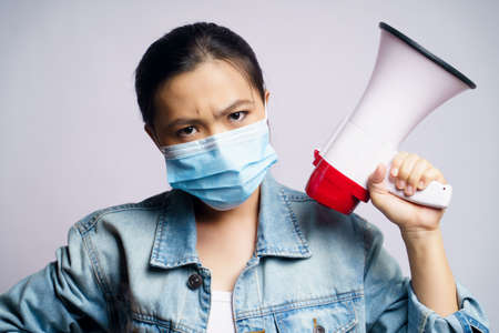Asian woman wearing protective face mask shouting with megaphone isolated on white background.の写真素材