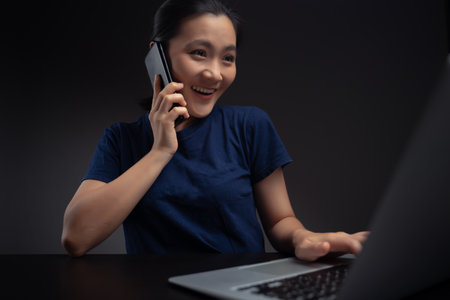 Asian woman working on laptop scans face by smart phone using facial recognition system.の写真素材