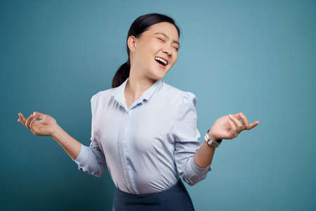 Asian woman happy confident standing showing her fist make a winning gesture isolated on blue background.の写真素材