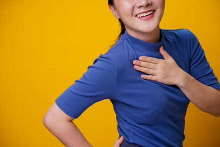 Happy Asian woman showing toothy smile standing isolated over yellow background.の写真素材