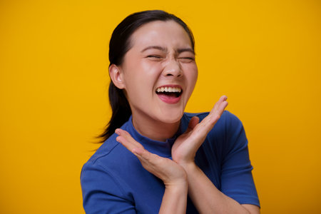 Happy Asian woman showing toothy smile standing isolated over yellow background.の写真素材