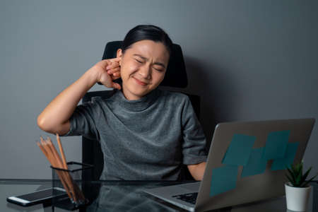 Asian woman working on a laptop was sick with stomach ache sitting at office. isolated on gray background.の写真素材