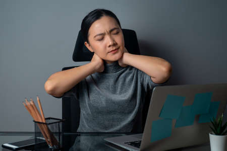 Asian woman working on a laptop was sick with stomach ache sitting at office. isolated on gray background.の写真素材