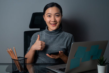 Asian woman happy smiling looking at copy space, working on a laptop at office. isolated on gray...