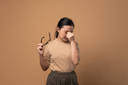 Asian woman bored and annoyed, scratching her head, standing isolated on beige background.