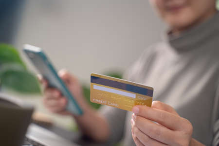 Close up shot of females hands holding credit card typing message on smart phone for shopping online at home office.の写真素材