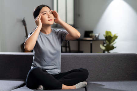 Asian woman was sick with body pain touching her body sitting on sofa in living room at home.の写真素材