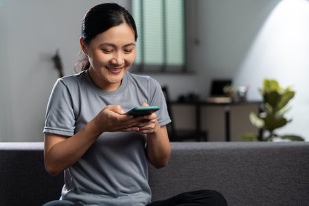 Happy woman with headphones and listening to music sitting on sofa in living room at home.の写真素材