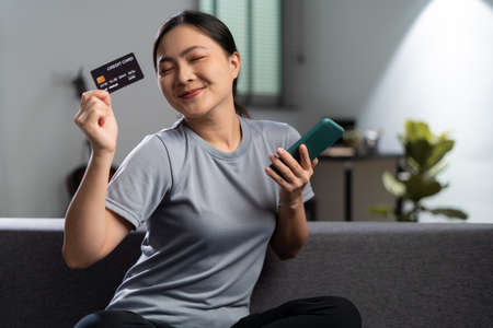 Happy woman with headphones and listening to music sitting on sofa in living room at home.の写真素材