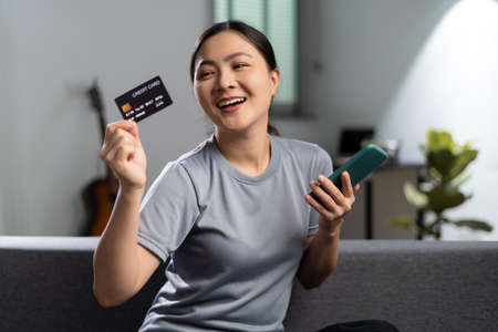 Happy woman with headphones and listening to music sitting on sofa in living room at home.の写真素材