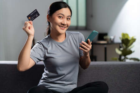 Happy woman with headphones and listening to music sitting on sofa in living room at home.の写真素材
