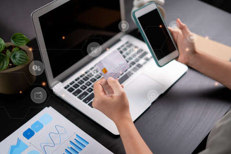 Close up shot of females hands holding credit card typing message on smart phone with technology icons for shopping online at home office.の写真素材