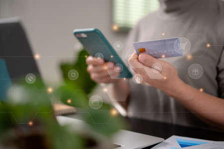 Close up shot of females hands holding credit card typing message on smart phone with technology icons for shopping online at home office.の写真素材