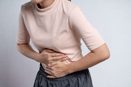 Asian woman was sick with stomach ache, putting her hands on her belly and standing isolated on white background.の写真素材