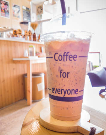 A glass of iced coffee and the concept words which tell us that coffee always be the source of energy for everyone. It is placed on a wooden saucer on a wooden table in a coffee shop.の写真素材