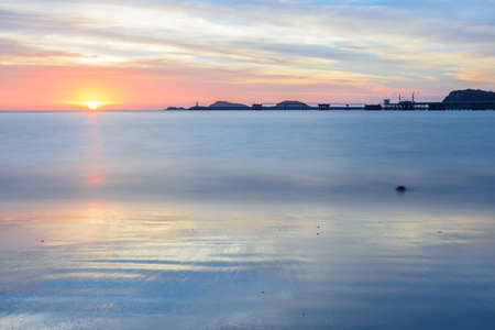 Beautiful seascape view when sunset at Nang Rum beach located in Chon Buri in eastern of Thailand with port, hill, lighthouse, cloud and twilight sky as background. Complementary color. Long exposure.のeditorial素材