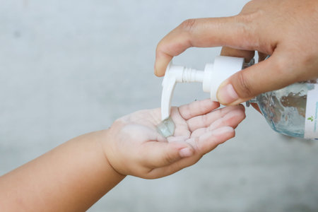 covid-19, asian mom pressing alcohol from a bottle to hand, little child girl washes her hands after playing in a park to prevent corona virusの写真素材