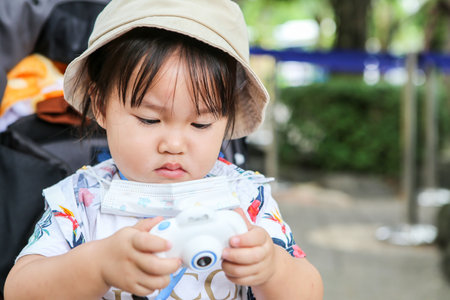 Cute Asian baby girl looking at her kid camera in the parkの写真素材