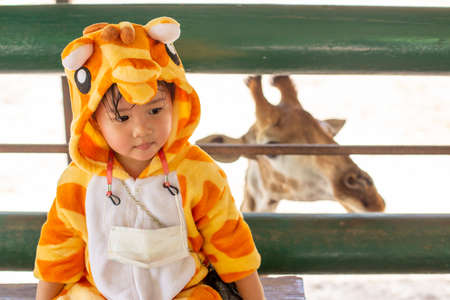 A cute Asian girl wearing a giraffe costume, Go on a trip in the zoo, Sitting and resting at the giraffe farm.の写真素材