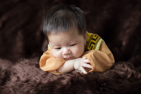 A newborn baby wearing a Chinese emperor's costume gold colour lying on a brown blanket.の写真素材