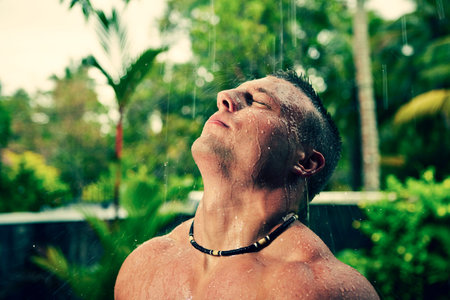 Muscular man is having shower in the rain.