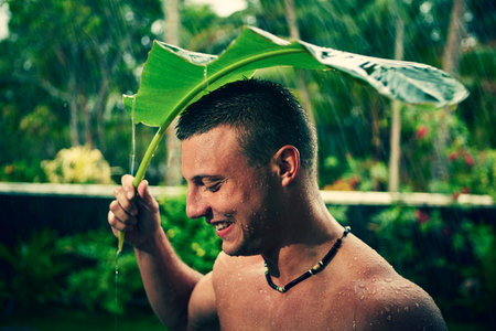 Muscular man is under the palm leaf in the rain.の写真素材
