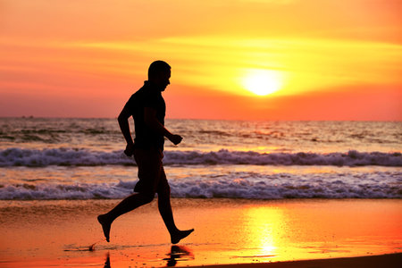 Young man is running on the beach at sunset.の写真素材