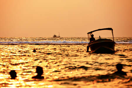 Fishing boat and silhouettes people in the sea - selective focusの写真素材