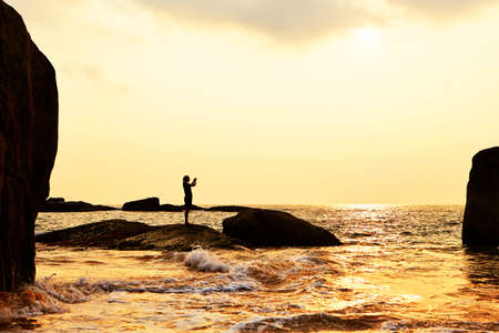 Silhouette of young woman with digital camera on the beach at sunset. の写真素材
