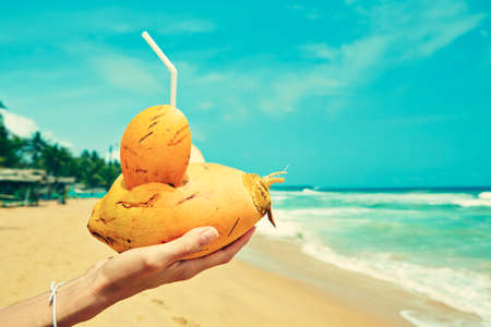 Hand of the woman with coconut drink on the beachの写真素材