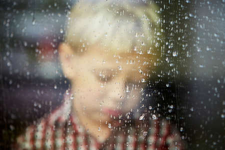 Little boy behind the window in the rain - selective focusの写真素材