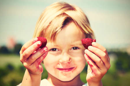 Little girl with fresh raspberries in natureの写真素材