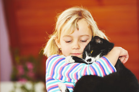 Little blond girl is playing with her black catの写真素材