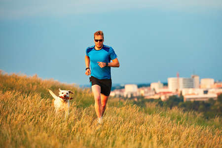 Sport lifestyle with dog. Athletic young man and labrador retriever are running on the hillside outside the city. Prague, Czech Republic.の写真素材