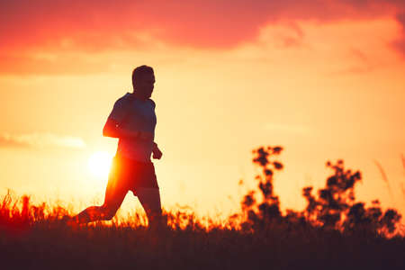 Silhouette of runner. Outdoor cross-country running. Athletic young man is running in the nature during golden sunset.の写真素材