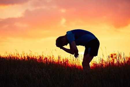 Silhouette of runner. Outdoor cross-country running. Pensive young man is taking rest after running in the nature during golden sunset.の写真素材