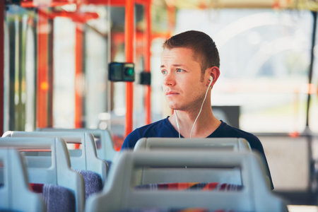 Sad young man is traveling by tram (bus). Everyday life and commuting to work by public transportation. Man is wearing headphones and listening to music.の写真素材