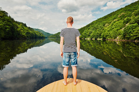Vacation trip on the river. Handsome man with blue and white striped shirt on the prow of the boat....