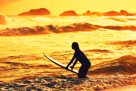 Silhouette of the beautiful surfer girl is enjoying vacation on the tropical beach. Young woman with...