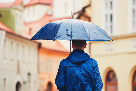 Rainy day. Young man is holding blue umbrella and walking in rain. Street of Prague, Czech Republic.