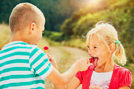 Children enjoying sunny day in holiday. Cheerful little boy and little girl tasting lollipops.の写真素材